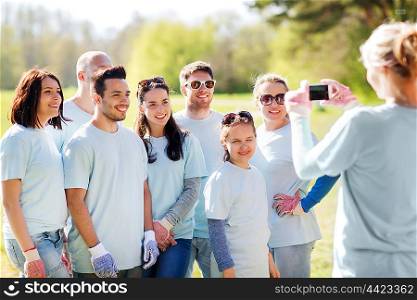 volunteering, charity, people, teamwork and environment concept - group of happy volunteers taking picture by smartphone in park