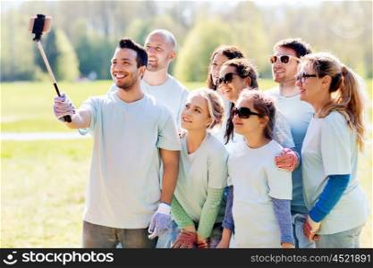 volunteering, charity, people, teamwork and environment concept - group of happy volunteers taking picture by smartphone and selfie stick in park