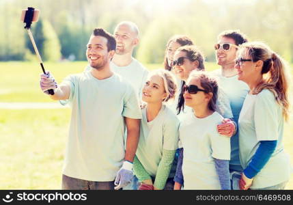 volunteering, charity, people, teamwork and environment concept - group of happy volunteers taking picture by smartphone and selfie stick in park. group of volunteers taking smartphone selfie