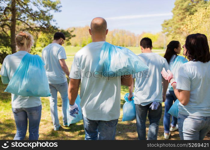 volunteering, people and ecology concept - group of happy volunteers with garbage bags walking after cleaning park area. group of volunteers with garbage bags in park