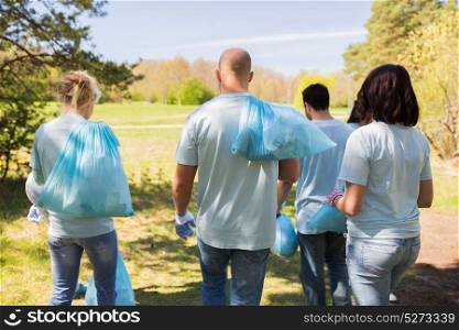 volunteering, people and ecology concept - group of volunteers with garbage bags walking after cleaning park area. group of volunteers with garbage bags in park
