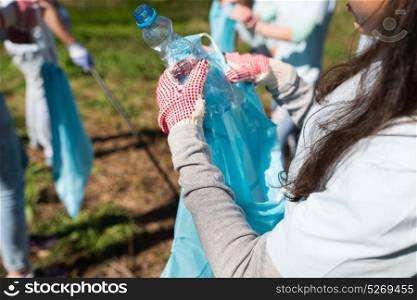 volunteering, people and ecology concept - volunteer woman with garbage bag and plastic bottle cleaning area in park. volunteer with trash bag and bottle cleaning area