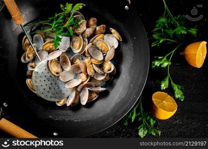 Vongole in a saucepan with lemon slices and parsley. On a black background. High quality photo. Vongole in a saucepan with lemon slices and parsley.