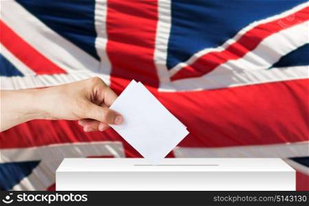 voting, civil rights and people concept - male hand putting his vote into ballot box on election over british flag background. hand of englishman with ballot and box on election