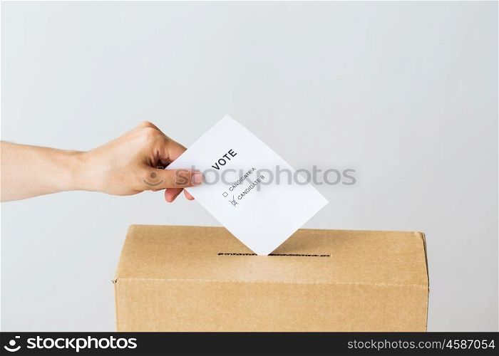 voting, civil rights and people concept - male hand putting vote with two candidates into ballot box on election