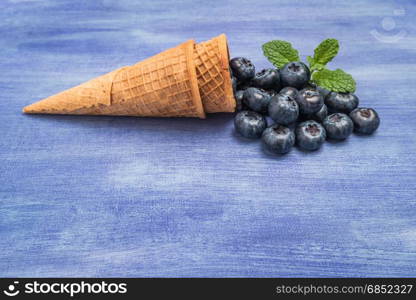 Waffle cones with blueberries and mint leaf on rustic textured background. Top view with copy space.