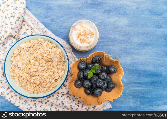 Waffle with blueberries and mint leaf. Yogurt and bowl of oatmeal on rustic textured background. Top view with copy space.