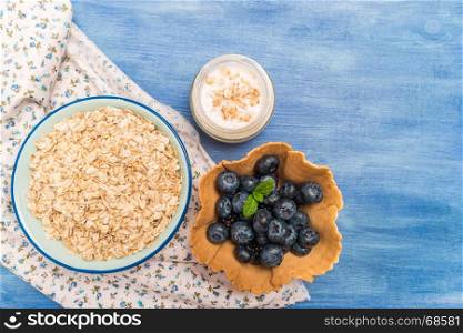 Waffle with blueberries and mint leaf. Yogurt and bowl of oatmeal on rustic textured background. Top view with copy space.