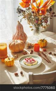 Waffles breakfast served on seasonal decorated autumn table with pumpkins, branch bouquet, autumn leaves and cutlery at window background with natural sunlight. Delicious sweet food. Front view.