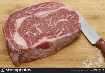Wagyu ribeye steak on a chopping board being seasoned with sea salt.