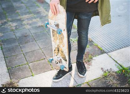 Waist down view of young male urban skateboarder standing on sidewalk