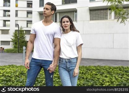 Waist up portrait of happy twosome holding hands and walking down the street. They curiously looking forward. House on background. Copy space on right side