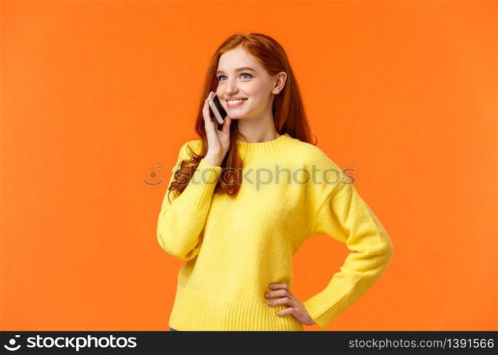 Waist-up portrait pretty redhead female calling friend, having conversation, confirm online order while shopping for holidays, standing carefree hold smartphone near ear, orange background.. Waist-up portrait pretty redhead female calling friend, having conversation, confirm online order while shopping for holidays, standing carefree hold smartphone near ear, orange background