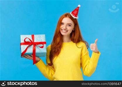 Waist-up shot satisfied good-looking redhead woman showing thumb-up in approval or like, love celebrating christmas holidays and receive gifts, holding bix box of present and wear fancy hat, smiling.. Waist-up shot satisfied good-looking redhead woman showing thumb-up in approval or like, love celebrating christmas holidays and receive gifts, holding bix box of present and wear fancy hat, smiling