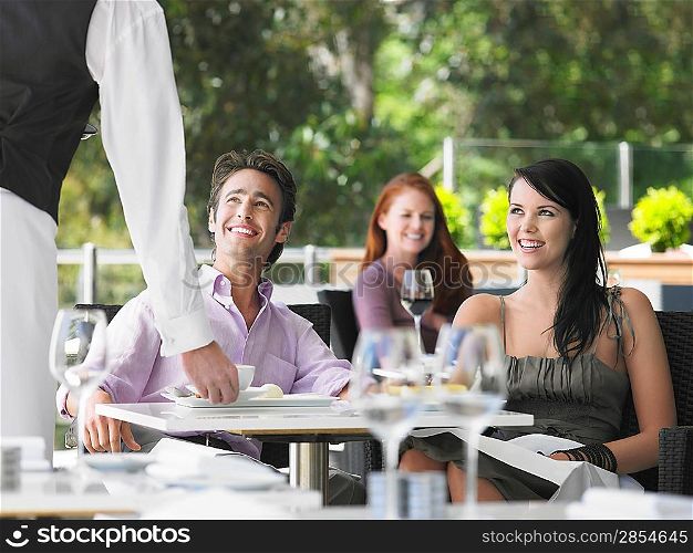 Waiter bringing coffee to couple at outdoor cafe