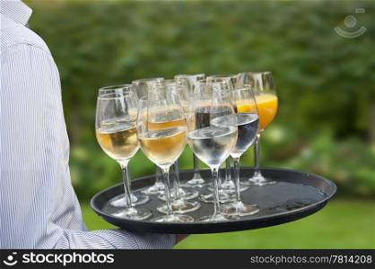 Waiter carrying a tray with wine glasses, orange juice and miniral water on an outdoors reception