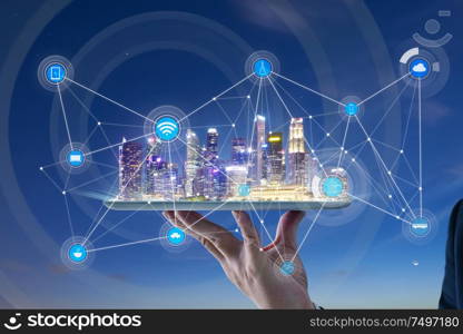 Waiter hand holding an digital tablet with Smart city with smart services and icons, internet of things, networks and augmented reality concept , night scene .