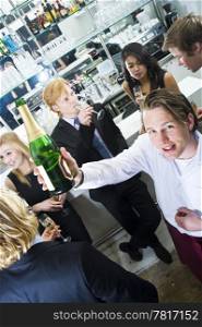 Waiter holding up a bottle of champagne, surrounded by a group of partying people