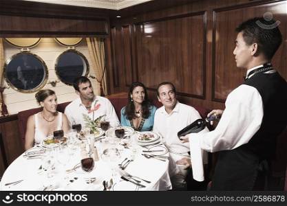Waiter serving wine bottle to two mid adult couples