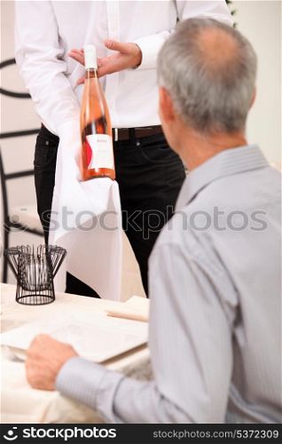 Waiter showing bottle of wine to man dining alone