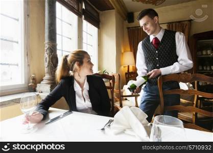Waiter showing wine bottle to female customer at table in restaurant