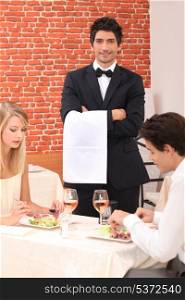 Waiter stood by couple enjoying meal
