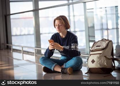waiting for a flight at the airport. girl with a phone and a backpack sits on the floor