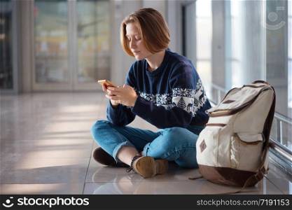 waiting for a flight at the airport. girl with a phone and a backpack sits on the floor