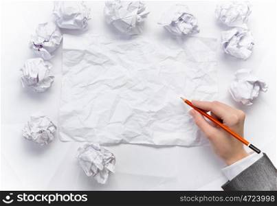 Waiting for inspiration. Hand of businesswoman writing on blank crumpled sheet of paper
