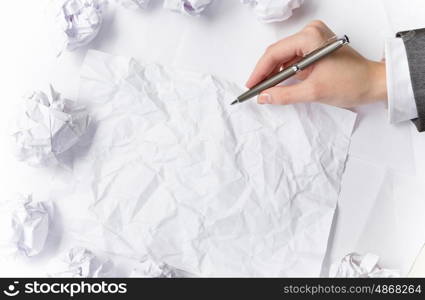 Waiting for inspiration. Hand of businesswoman writing on blank crumpled sheet of paper