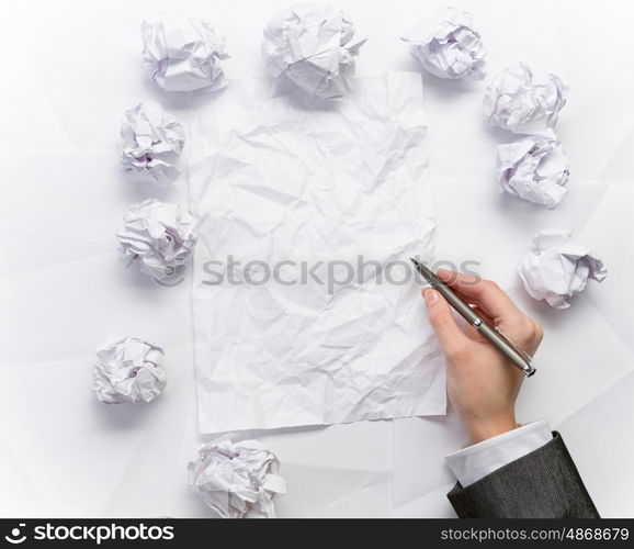 Waiting for inspiration. Hand of businesswoman writing on blank crumpled sheet of paper