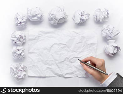 Waiting for inspiration. Hand of businesswoman writing on blank crumpled sheet of paper