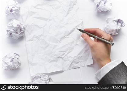Waiting for inspiration. Hand of businesswoman writing on blank crumpled sheet of paper