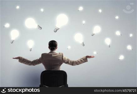 Waiting for inspiration to come. Young businesswoman sitting in chair and light bulbs above