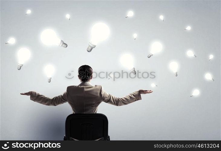 Waiting for inspiration to come. Young businesswoman sitting in chair and light bulbs above