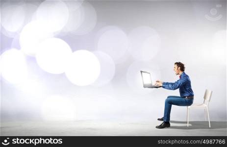 Waiting for inspiration!. Young man sitting in chair and using laptop