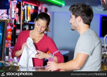 waitress cleaning glasses in a bar white talking to customer
