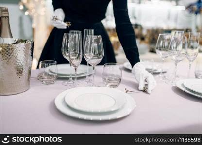Waitress in gloves puts the knife, table setting. Serving service, festive dinner decoration. Waitress in gloves puts the knife, table setting