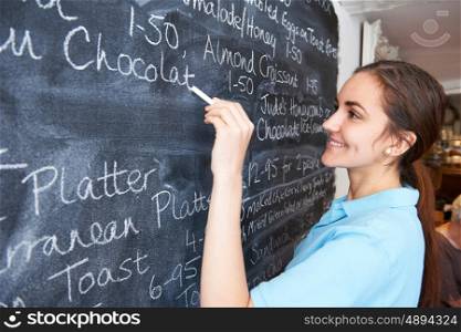 Waitress In Restaurant Writing Menu On Blackboard