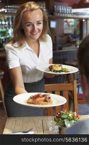 Waitress Serving Customer Sitting At Table In Restaurant