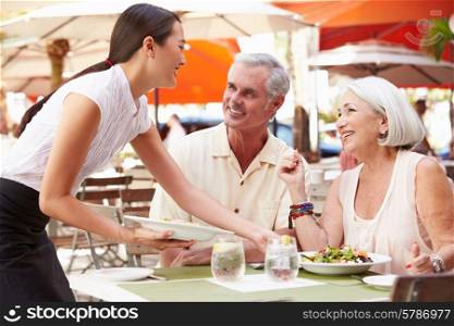 Waitress Serving Senior Couple Lunch In Outdoor Restaurant