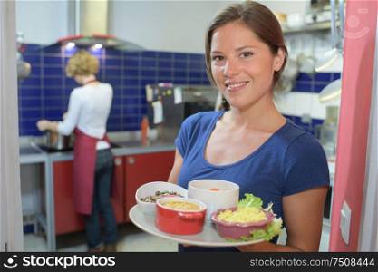 waitress showing dishes to the camera and chef in background