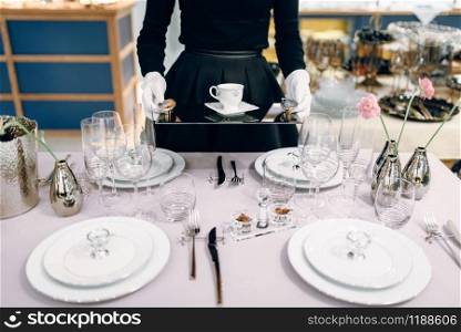 Waitress with a tray puts the dishes, table setting. Serving service, festive dinner decoration, holiday dinnerware. Waitress with tray puts the dishes, table setting