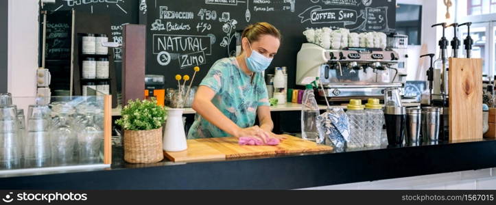 Waitress with mask disinfecting the bar counter due to coronavirus. Waitress disinfecting bar counter due to coronavirus