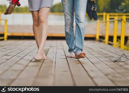 Walk along the boardwalk by the lake.. Young man and girl walking barefoot on the planks of the pier 6542.