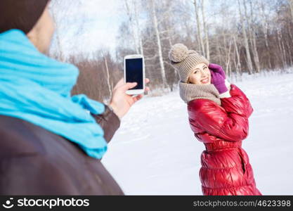 Walk in winter park. Young man in winter park making photo of his girlfriend