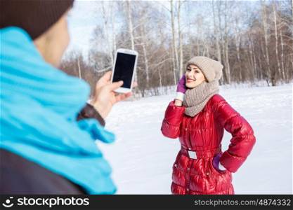 Walk in winter park. Young man in winter park making photo of his girlfriend
