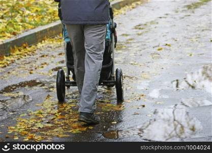 Walking father with child in the fresh air. A man carries a baby carriage on an asphalt road, through puddles.