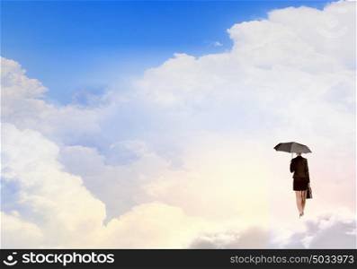 Walking on clouds. Young businesswoman with black umbrella standing on cloud