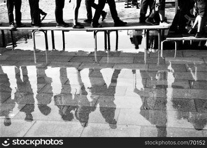 Walking people reflect in a puddle on San Marco square in Venice, Italy. Black and white image